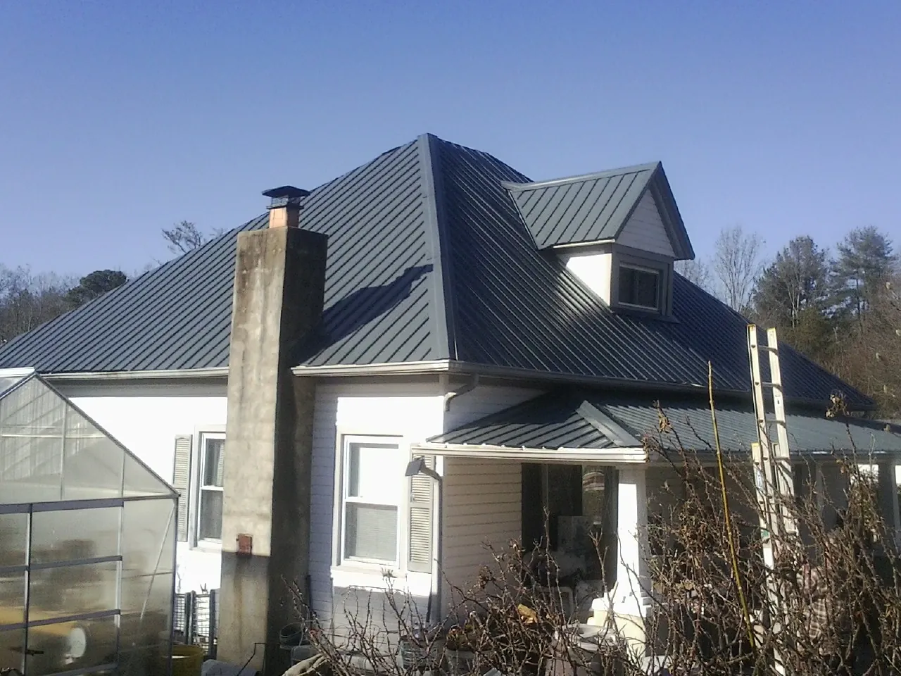 Dark blue standing seam metal roof on a white farmhouse with dormer — Slate & Tile Roof Repair by Roofing Brothers in Goehner