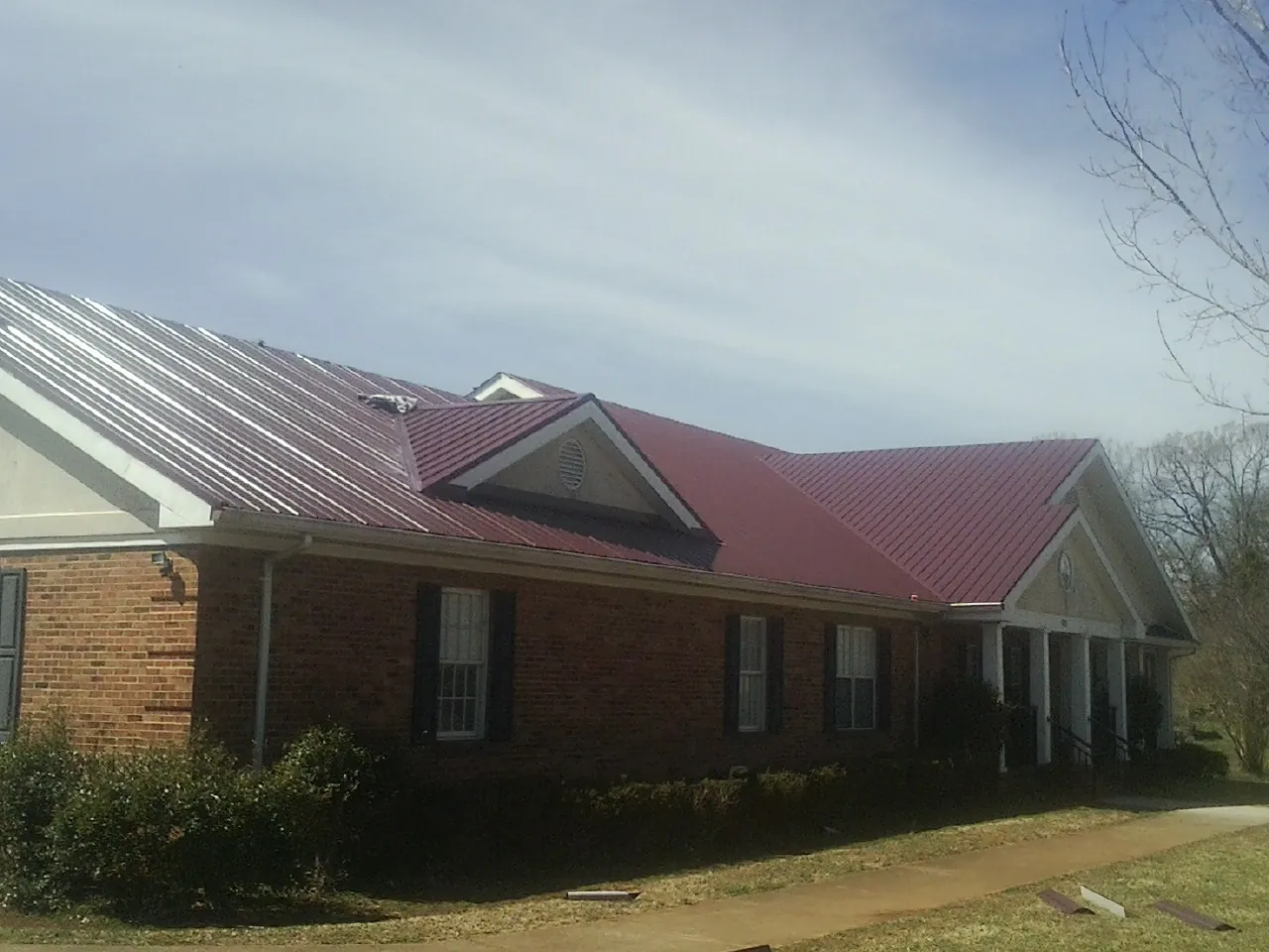 Red metal roof with gabled entries on a long brick building, from a Hail Damage Roof Repair job in Goehner