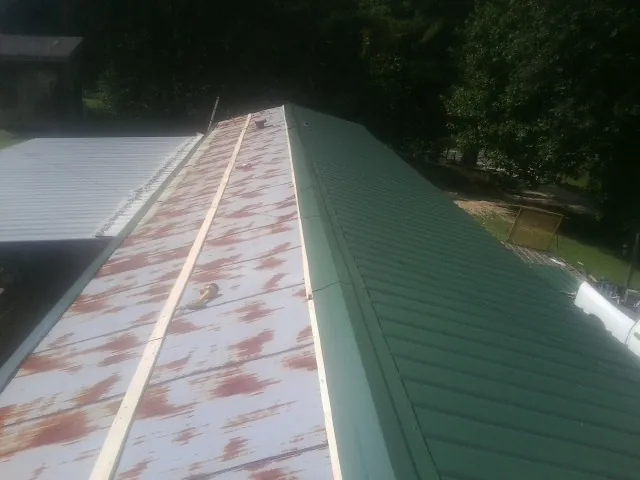 Old rusted panels beside newly installed green metal roofing — Wind Damage Roof Repair by Roofing Brothers in Goehner