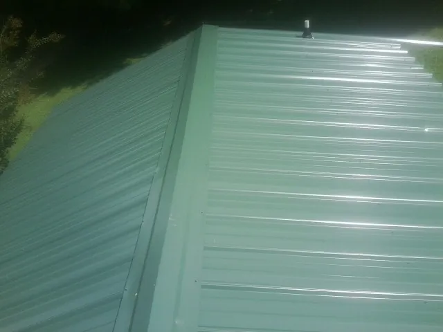 New green metal panels meeting at the ridge of a roof — Flat Roof Repair work by our crew in Goehner