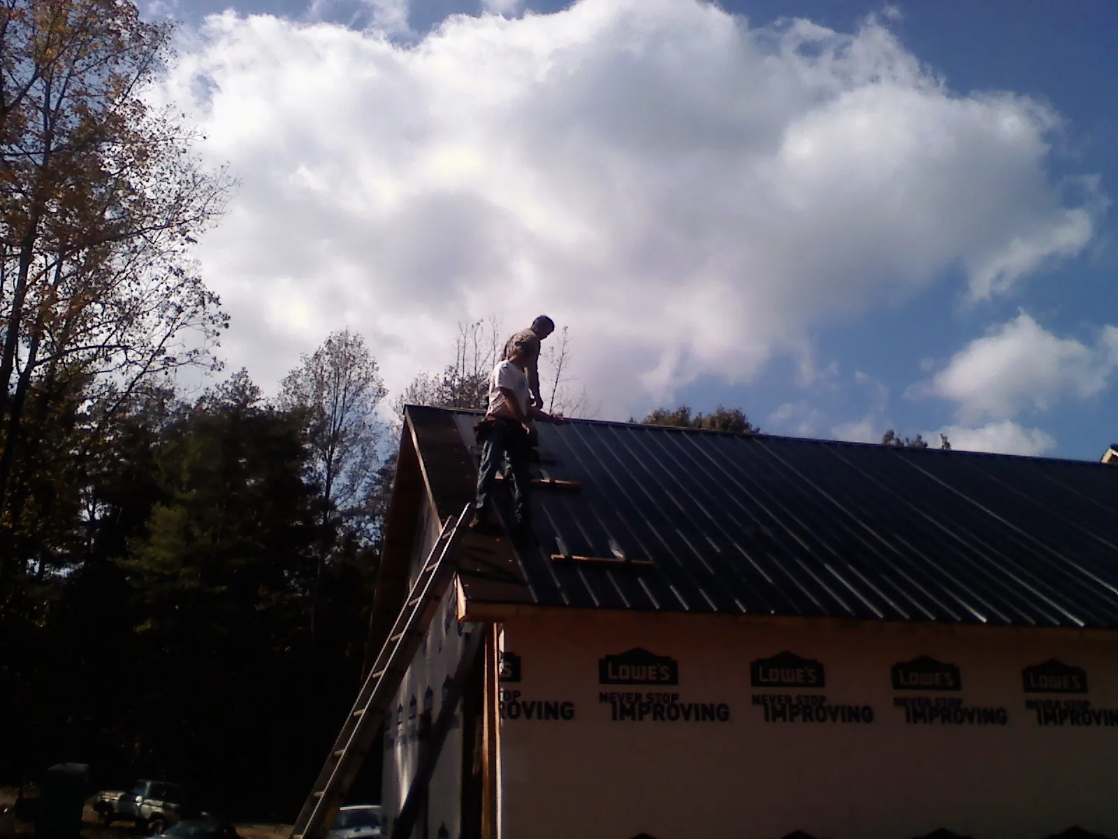 Roofer fastening dark metal panels high against a cloudy sky, from a Roof Inspection job in Goehner