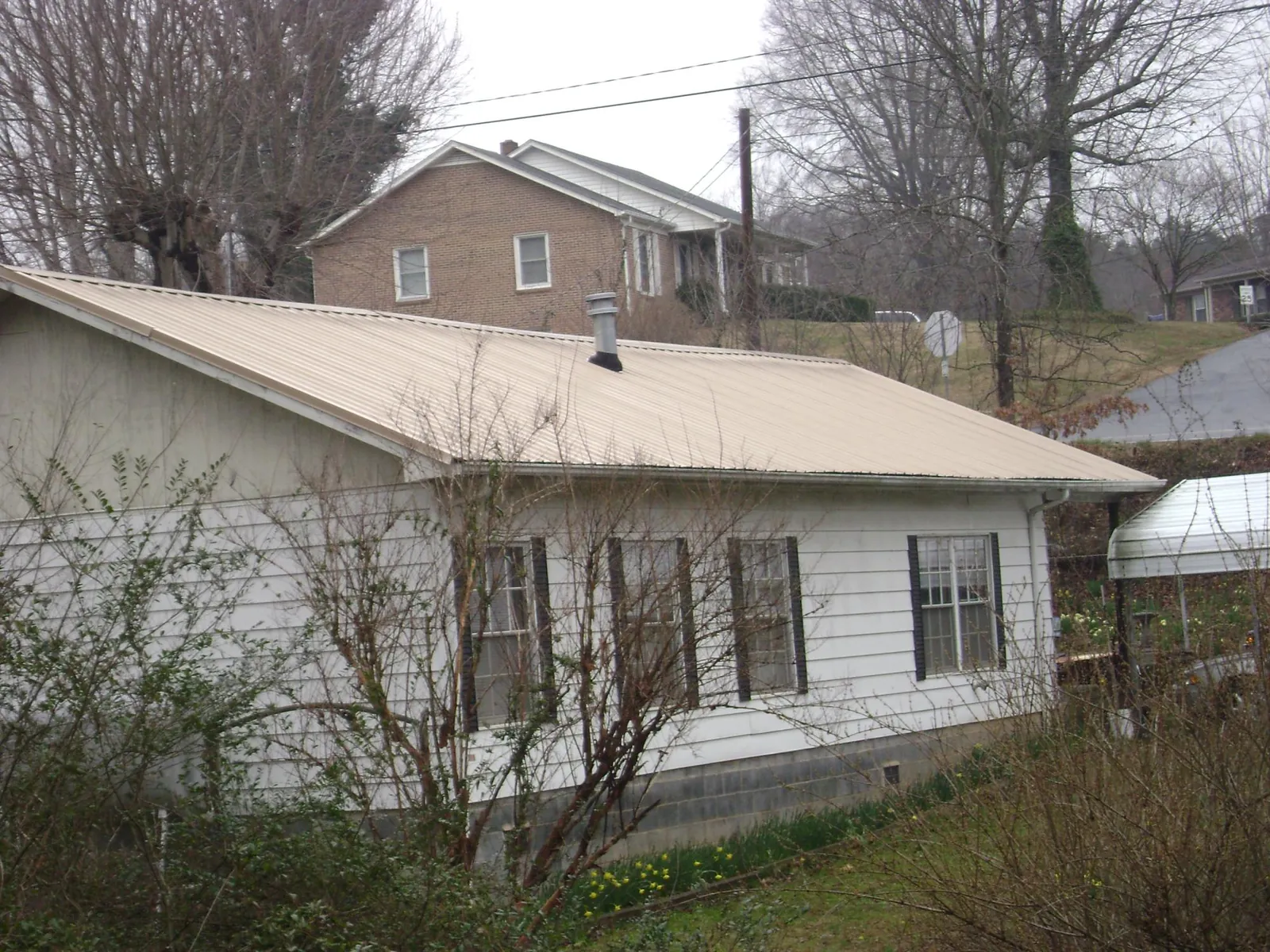Tan metal roof on a white sided house set into a hillside — Commercial Roofing by Roofing Brothers in Goehner