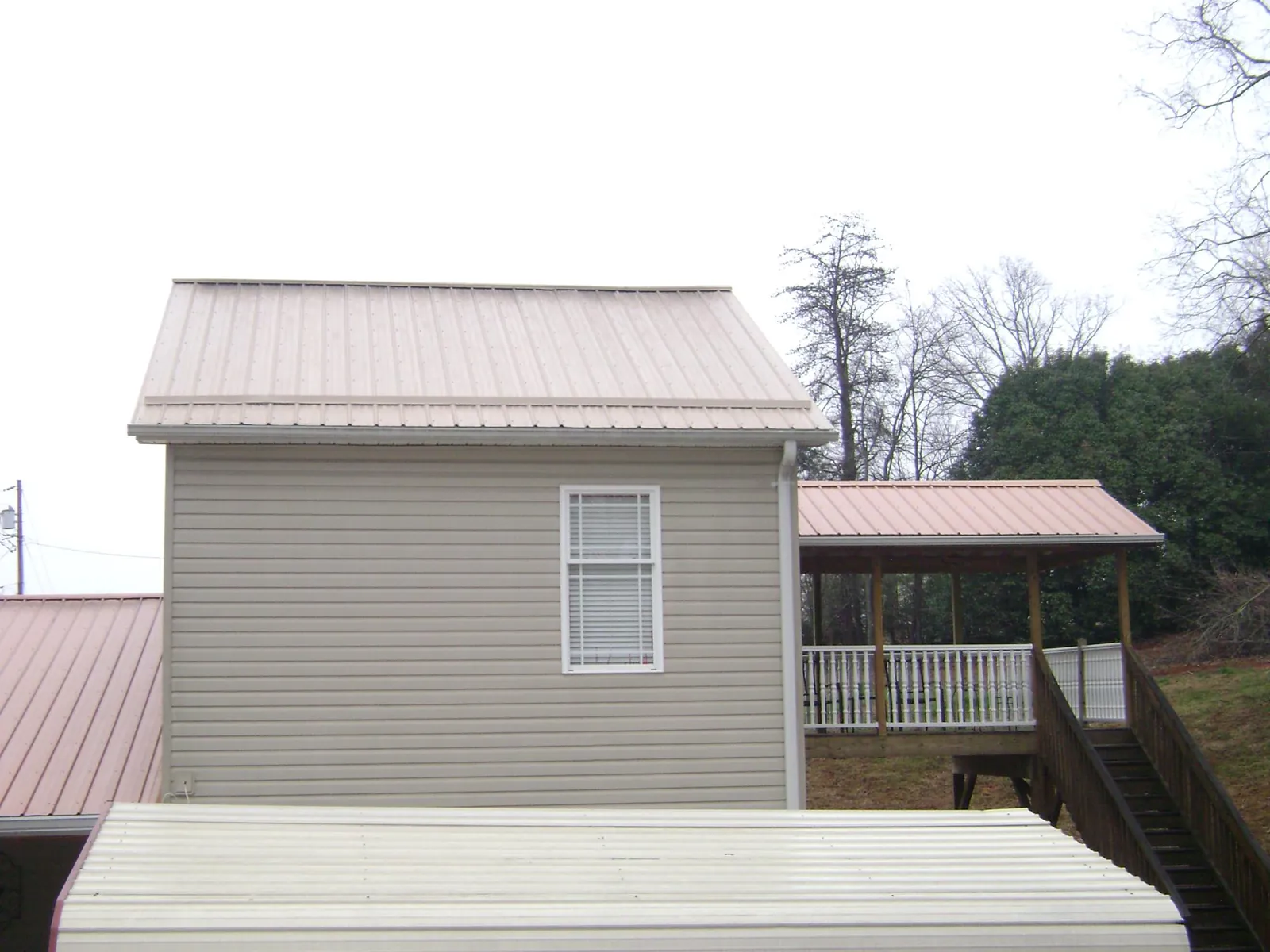 Tan metal roofs on a two story addition and attached porch, from a Roof Replacement job in Goehner